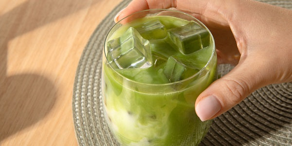 Hand hält Iced Matcha Glas mit Eiswürfeln