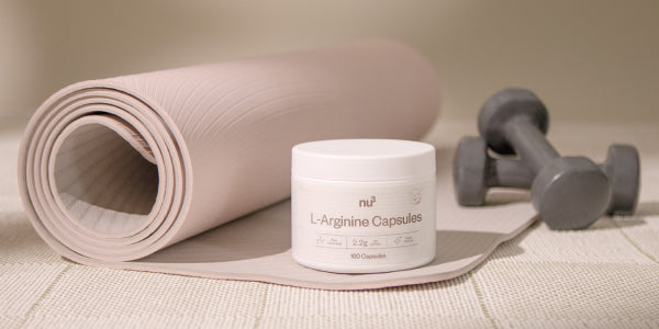 Arginin-Kapseln liegen vor einer Yogamatte und Hanteln