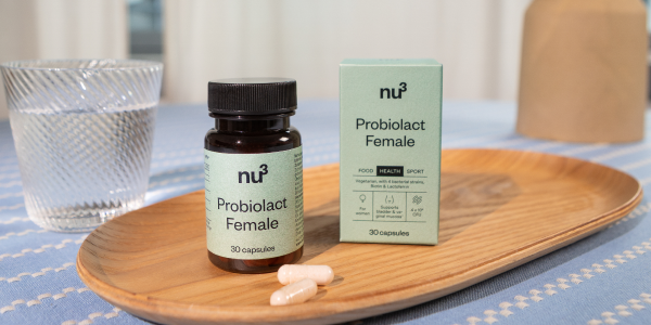 Probiotlact Dose und Verpackung auf einem Holztablett mit einem Glas Wasser und zwei Kapseln