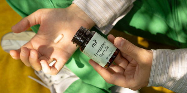 Eine Dose Probiolact female in der Hand und zwei Kapseln in der anderen Hand