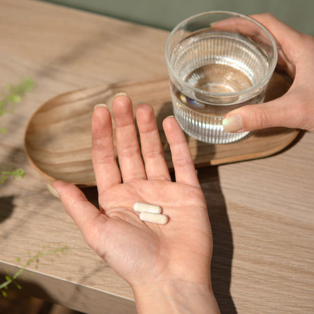 Kapseln in der Hand mit Glas Wasser