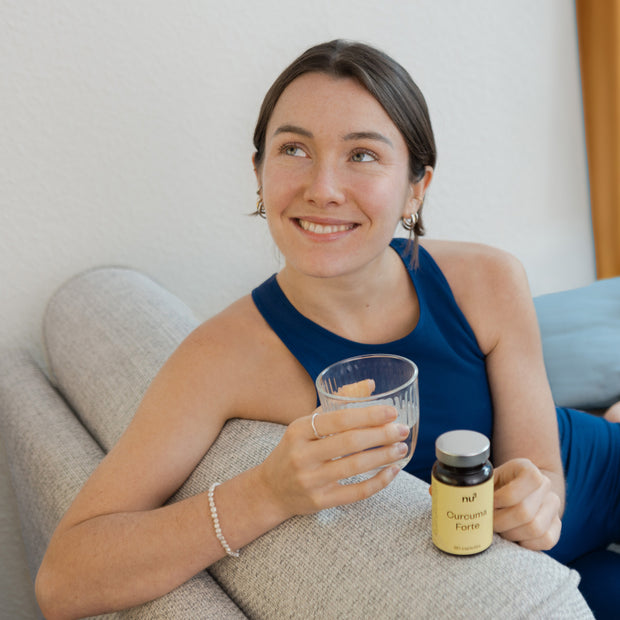 Frau mit Kurkuma Kapseln und Glas Wasser auf dem Sofa